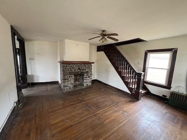unfurnished living room with stairway, a ceiling fan, baseboards, wood-type flooring, and a brick fireplace