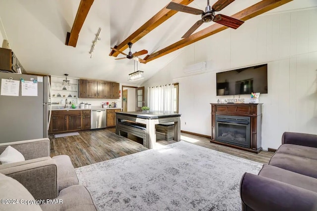 living room featuring beam ceiling, a wall unit AC, a ceiling fan, a glass covered fireplace, and wood finished floors