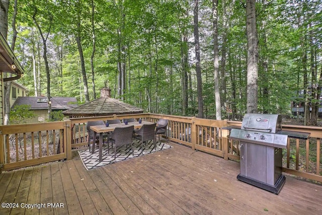 deck featuring outdoor dining area, a view of trees, and area for grilling