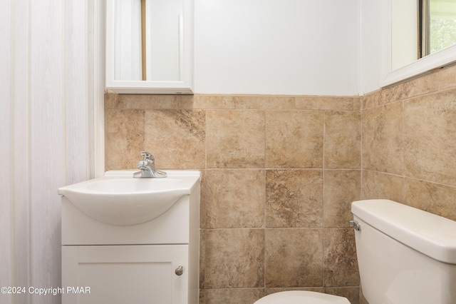 bathroom with toilet, tile walls, and vanity