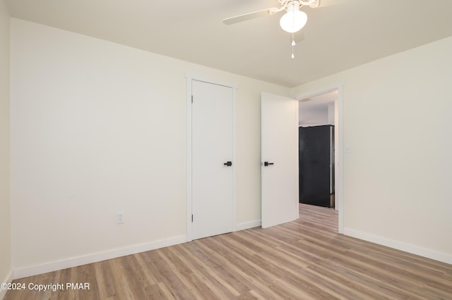 unfurnished bedroom featuring a ceiling fan, freestanding refrigerator, light wood-style flooring, and baseboards