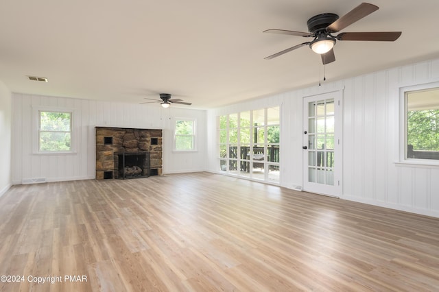 unfurnished living room featuring ceiling fan, a stone fireplace, light wood-type flooring, and visible vents