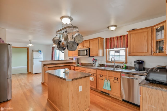 kitchen with stainless steel appliances, a center island, a peninsula, a sink, and dark countertops