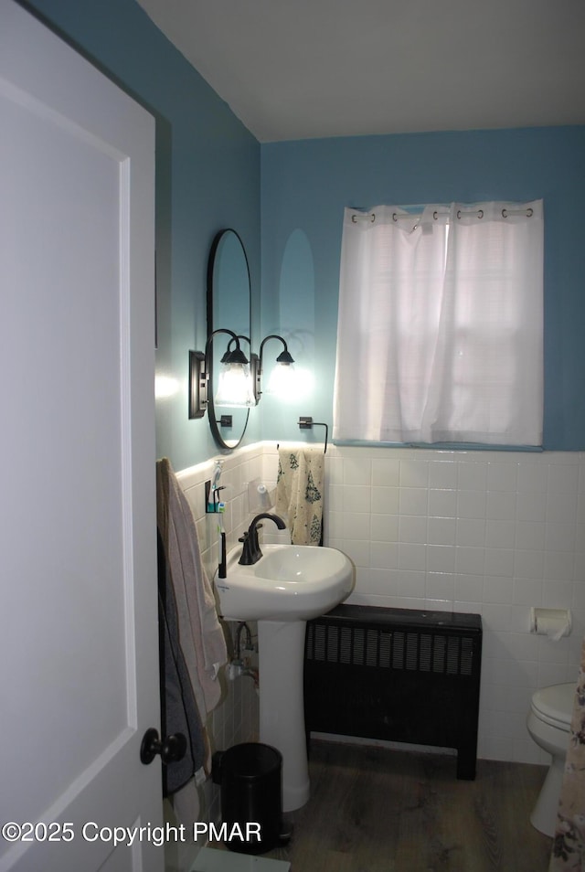 bathroom with radiator heating unit, hardwood / wood-style floors, tile walls, and toilet