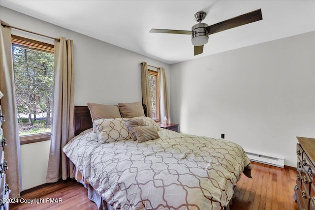 bedroom with ceiling fan, baseboard heating, and wood finished floors