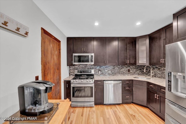 kitchen with a sink, stainless steel appliances, light wood-type flooring, and decorative backsplash