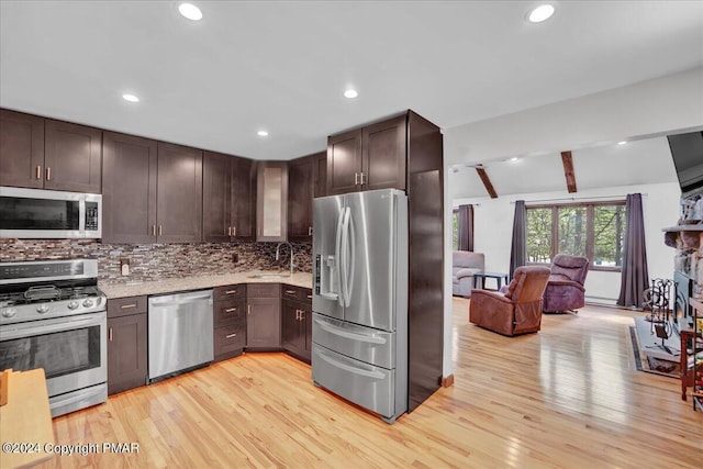 kitchen featuring dark brown cabinets, open floor plan, decorative backsplash, appliances with stainless steel finishes, and light wood-style floors