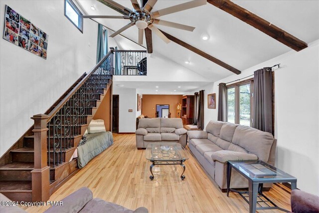 living area featuring stairs, beam ceiling, wood finished floors, and a ceiling fan