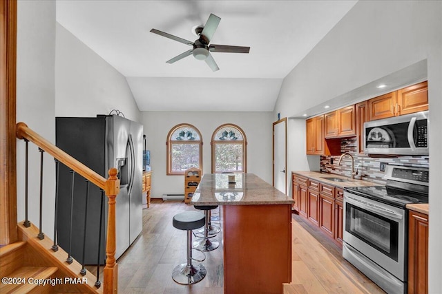 kitchen featuring lofted ceiling, a sink, stainless steel appliances, a kitchen bar, and a center island