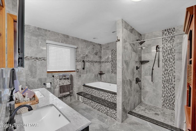 bathroom with a sink, tile walls, double vanity, a relaxing tiled tub, and tiled shower