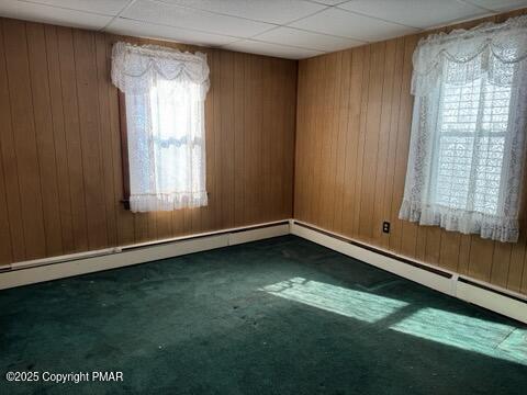 empty room featuring dark carpet, a paneled ceiling, and wood walls