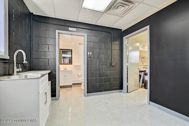 bathroom with concrete block wall, visible vents, toilet, vanity, and a paneled ceiling