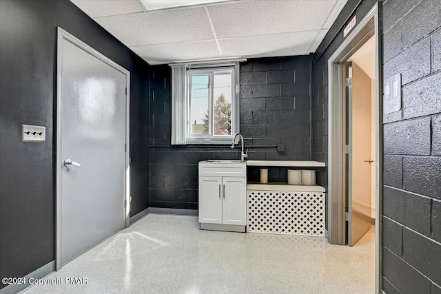 bathroom with concrete block wall, a drop ceiling, a sink, and speckled floor