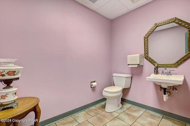 bathroom featuring baseboards, a drop ceiling, toilet, tile patterned flooring, and a sink