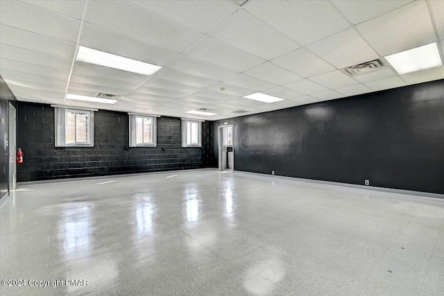 unfurnished room with a drop ceiling, visible vents, and concrete block wall