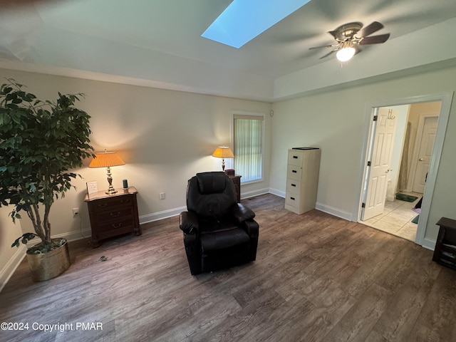 living area with baseboards, a skylight, a ceiling fan, and wood finished floors