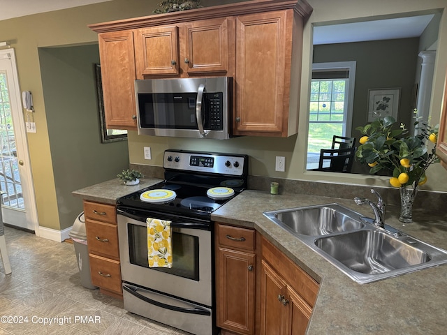 kitchen with brown cabinetry, appliances with stainless steel finishes, baseboards, and a sink