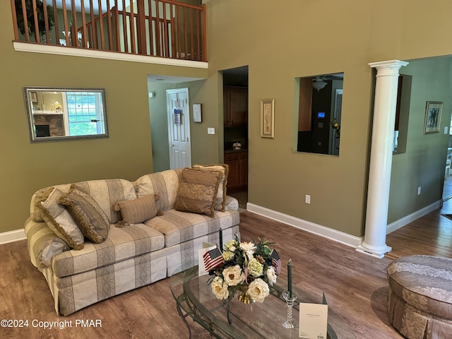 living area with ornate columns, a high ceiling, baseboards, and wood finished floors