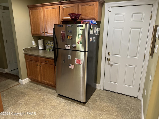 kitchen featuring dark countertops, baseboards, brown cabinets, and freestanding refrigerator