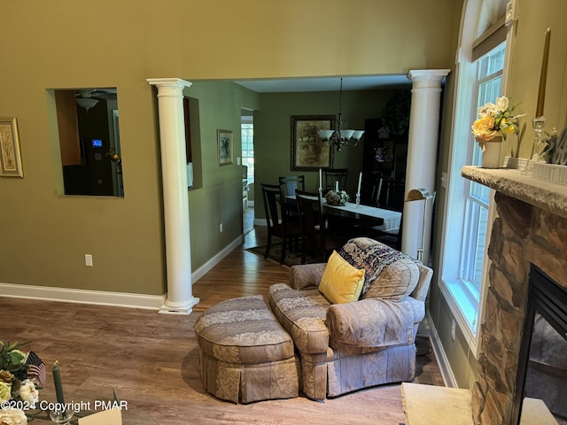 living room featuring baseboards, a stone fireplace, wood finished floors, and ornate columns