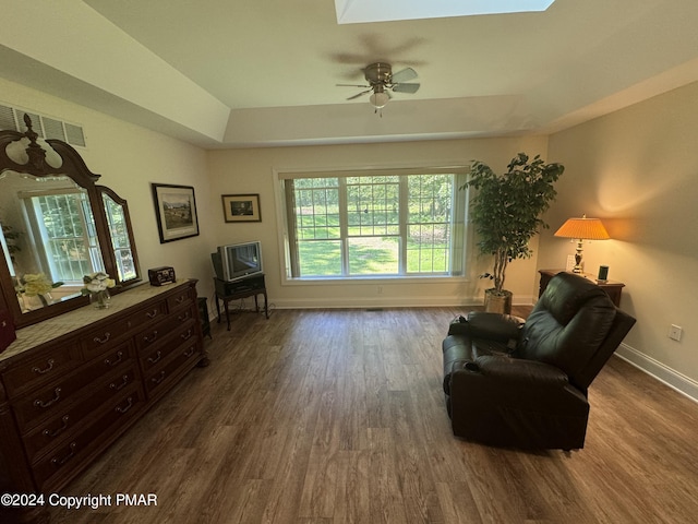 living area featuring visible vents, a raised ceiling, wood finished floors, baseboards, and ceiling fan