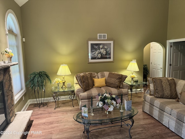 living area featuring wood finished floors, visible vents, baseboards, arched walkways, and a stone fireplace