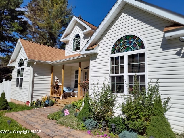 exterior space with covered porch, a shingled roof, and fence