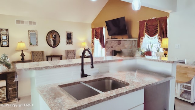 kitchen featuring lofted ceiling, light stone countertops, visible vents, and a sink