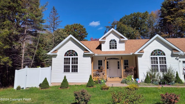 traditional home featuring a porch, a front yard, fence, and a shingled roof