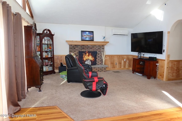 living room featuring vaulted ceiling, a brick fireplace, an AC wall unit, wooden walls, and carpet flooring