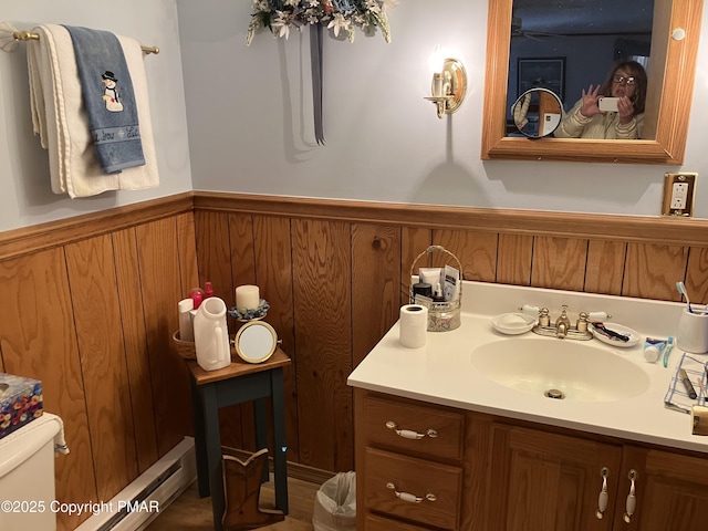 bathroom with wooden walls, a wainscoted wall, toilet, vanity, and a baseboard radiator