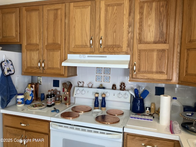 kitchen featuring light countertops, brown cabinetry, under cabinet range hood, and white range with electric stovetop