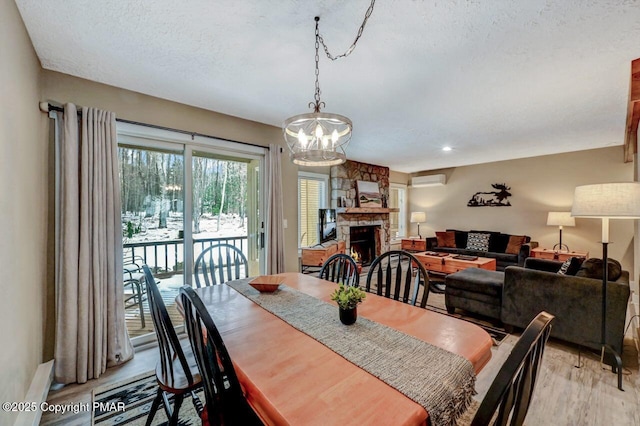 dining room featuring a wall mounted air conditioner, a stone fireplace, a textured ceiling, and light wood-type flooring