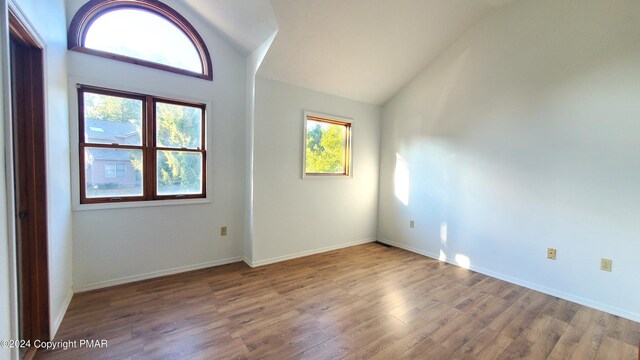 spare room with vaulted ceiling, baseboards, and wood finished floors