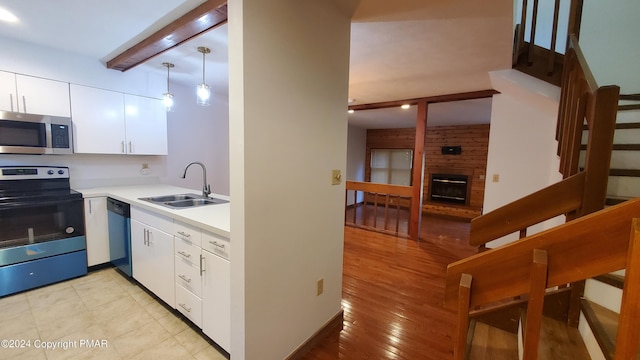 kitchen with electric range oven, stainless steel microwave, beamed ceiling, a brick fireplace, and a sink