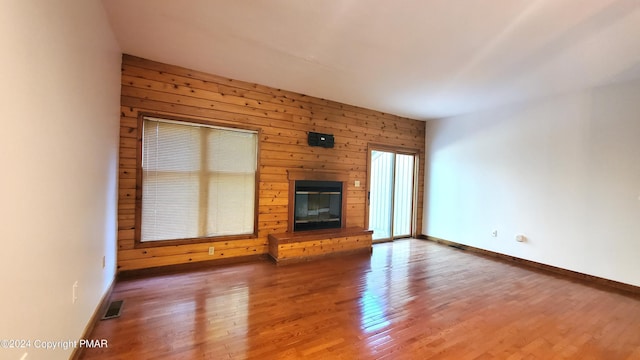 unfurnished living room with wooden walls, baseboards, visible vents, a glass covered fireplace, and wood finished floors