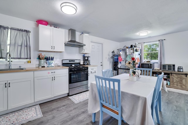 418 Leander Rd, East Stroudsburg, PA 18302 - kitchen featuring wall chimney exhaust hood, stainless steel gas stove, a sink, light wood-style floors, and white cabinetry