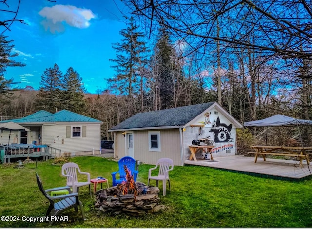 back of property with a deck, an outdoor structure, a yard, and a fire pit