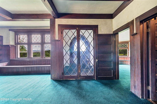 entrance foyer with beam ceiling, wood walls, and dark carpet