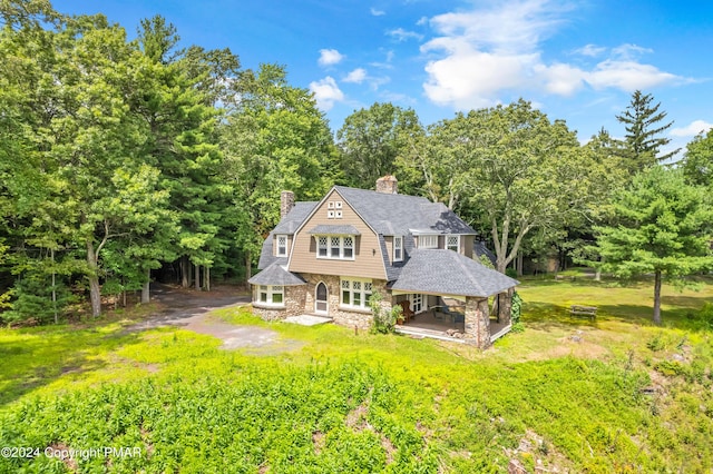 back of property with a gambrel roof, stone siding, a patio, a yard, and a chimney