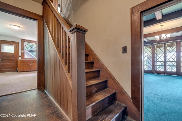 stairway with a notable chandelier, carpet flooring, wood-type flooring, and beam ceiling