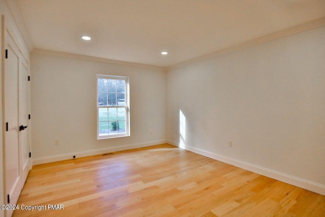 empty room with light wood-type flooring, baseboards, and crown molding