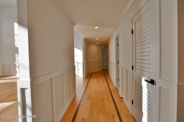 hall featuring crown molding, recessed lighting, a decorative wall, light wood-style floors, and wainscoting