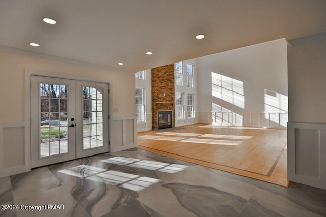 unfurnished living room with french doors, a wainscoted wall, crown molding, a fireplace, and a decorative wall