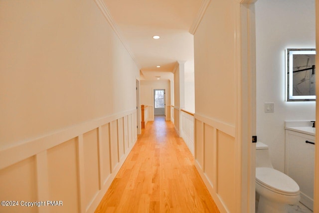 corridor with recessed lighting, a wainscoted wall, a decorative wall, ornamental molding, and light wood finished floors