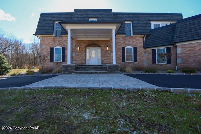 view of exterior entry with mansard roof and brick siding