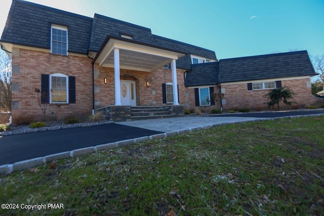 exterior space featuring a yard, brick siding, and mansard roof