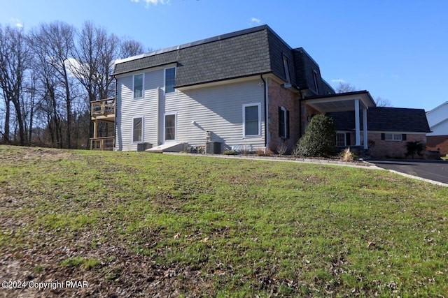 view of property exterior with a shingled roof, mansard roof, a lawn, cooling unit, and brick siding