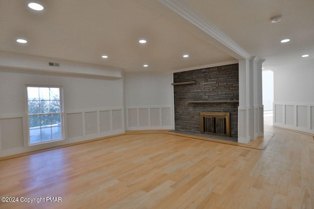 unfurnished living room with crown molding, a fireplace, visible vents, a decorative wall, and wood finished floors