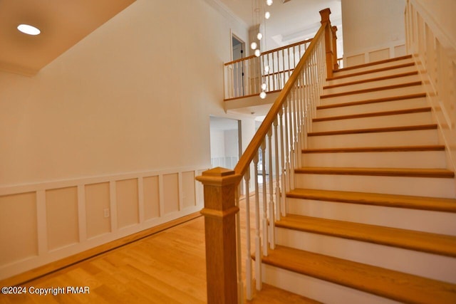 stairway with ornamental molding, recessed lighting, wood finished floors, and a decorative wall